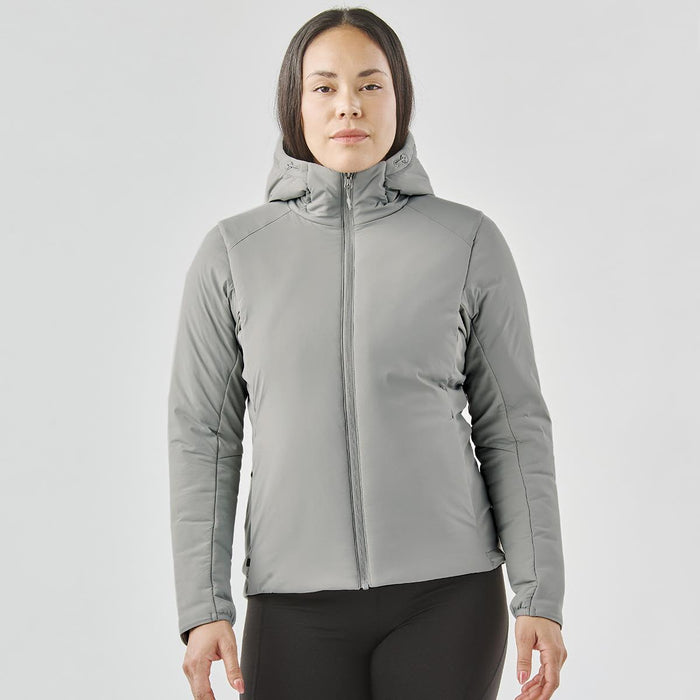 Women's Cascadia Thermal Jacket - A woman is wearing a grey puffer jacket with a hood. The jacket has a fitted design and features a logo.
