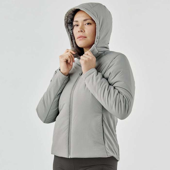 Women's Cascadia Thermal Jacket - A woman is wearing a grey puffer jacket with a hood, featuring a zip-up front and a fitted silhouette.