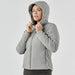 Women's Cascadia Thermal Jacket - A woman is wearing a grey puffer jacket with a hood, featuring a zip-up front and a fitted silhouette.