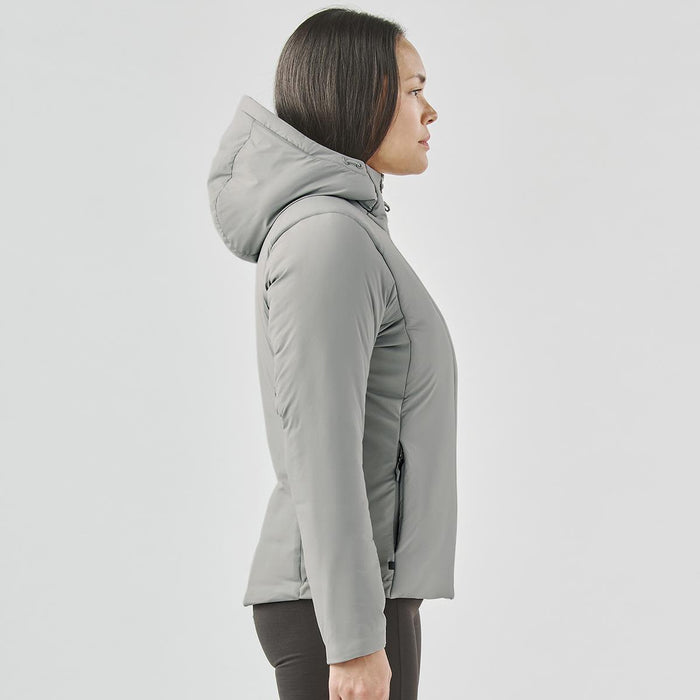 Women's Cascadia Thermal Jacket - A woman in a light grey puffer jacket with a hood, standing in profile. The jacket features a fitted design.