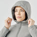 Women's Cascadia Thermal Jacket - A woman wearing a light grey thermal puffer jacket with a hood, adjusting it around her face.