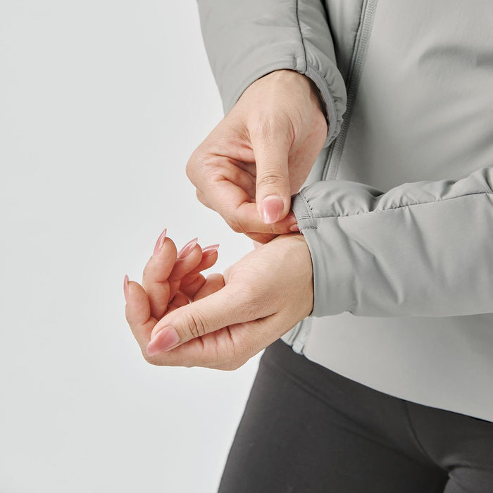 Women's Cascadia Thermal Jacket - A woman's hand adjusts the cuff of a light grey thermal jacket. The jacket features a fitted design with a logo.
