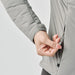 Women's Cascadia Thermal Jacket - A hand adjusting the zipper of a light grey women's puffer jacket, featuring a sleek design and logo.