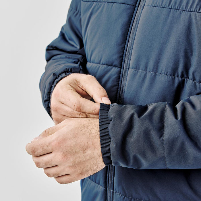 Men's Sierra Thermal Jacket - A navy blue puffer jacket featuring elastic cuffs, shown with hands adjusting the sleeve. The jacket has a logo.