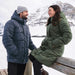 Women's Elkridge Parka - A man in a navy puffer jacket and a woman in a green puffer coat stand together outdoors in a snowy landscape.
