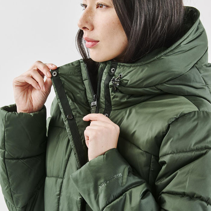 Women's Elkridge Parka - A woman in a green puffer jacket adjusts the zipper, showcasing the jacket's high collar and insulation.