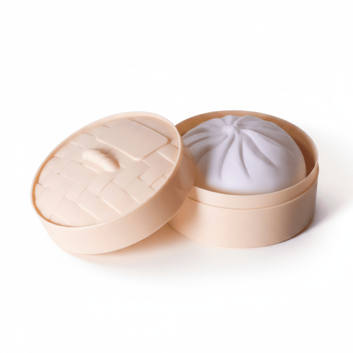 Squishy Bun - A squishy bun toy in a light peach round container with a lid, resembling a dim sum steamer.