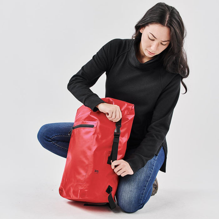 Cirrus Backpack 35 - A red backpack with a sleek design, featuring a zippered pocket and adjustable straps, held by a person in black attire.
